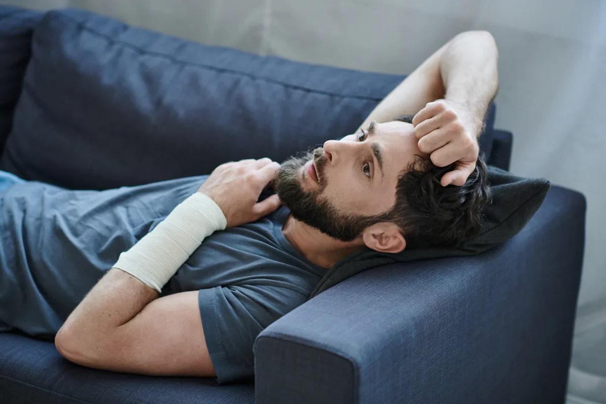 self-harm-why-it-happens-and-what-helps Person reclining alone on couch, with bandage on their arm, reflecting on self-harm and the path toward healing